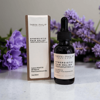 Taryn Philip Synergistic Pain Relief oil bottle and packaging with purple flowers in the background